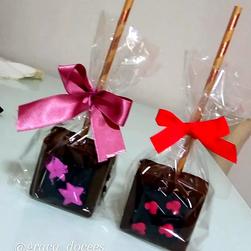Dois pirulitos de chocolate decorados com estrelas e corações, com laços